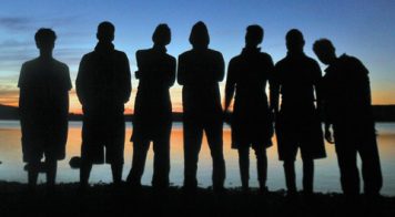 Silhouette-of-students-standing-on-shore-with-sunset-in-background