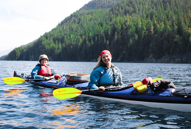 Image of two smiling people kayaking in the vibrant blue sea