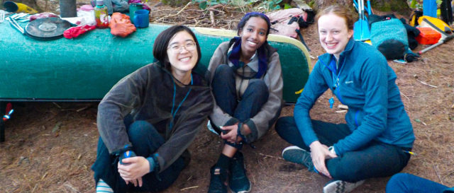 Image of grinning teens sitting in front of canoe