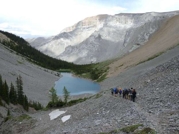 Group in the distance walking along a mountain path with a lake at the bottom