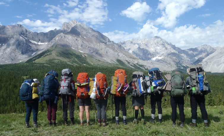 Ten people with hiking backpacks looking out at Mountains