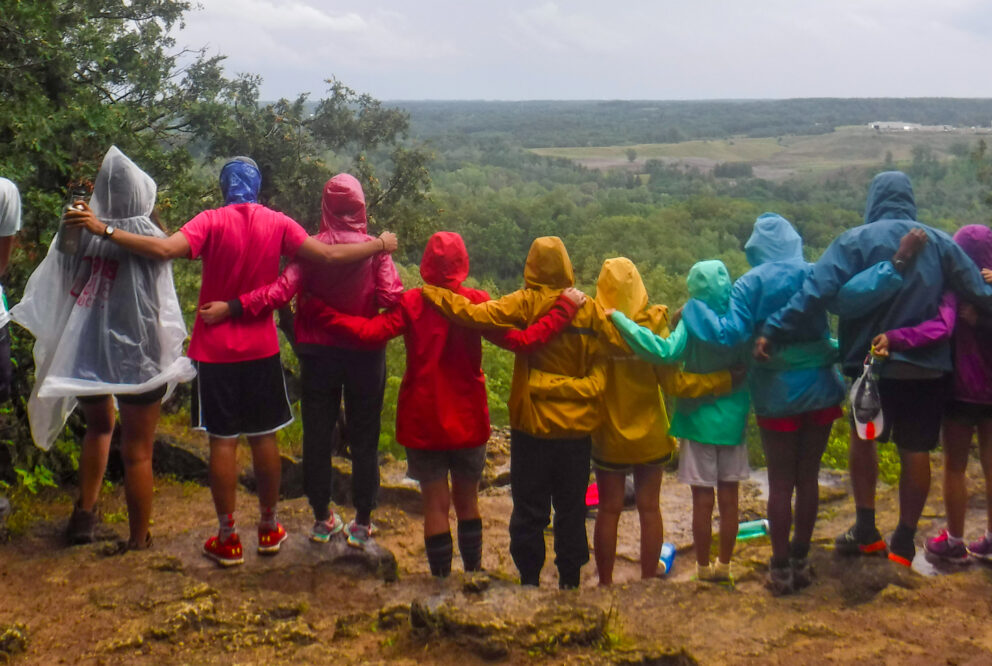 Group of people linked arms in rainbow-coloured rain jackets