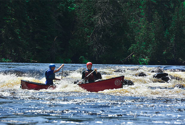 Image of two persons in red canoe paddling whitewater