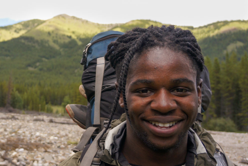 A backpacker smiling with mountains behind them.