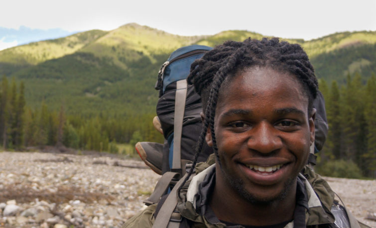 A backpacker smiling with mountains behind them.