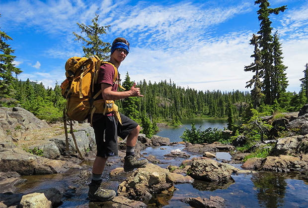 Image of a hiker showing a surf's up sign in front of a lake