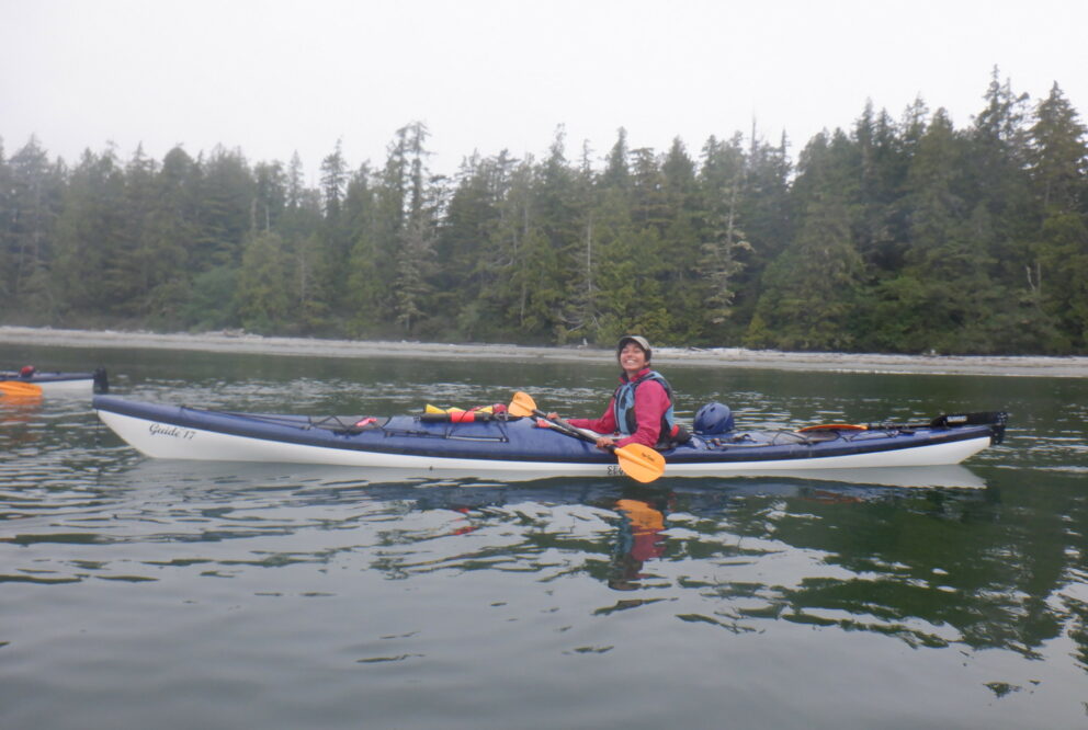 Young BIPOC female outdoor guide Shams Ben Temessek paddles a kayak in a lake