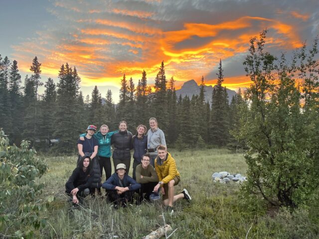 teens smiling in a forest with sunset in the background