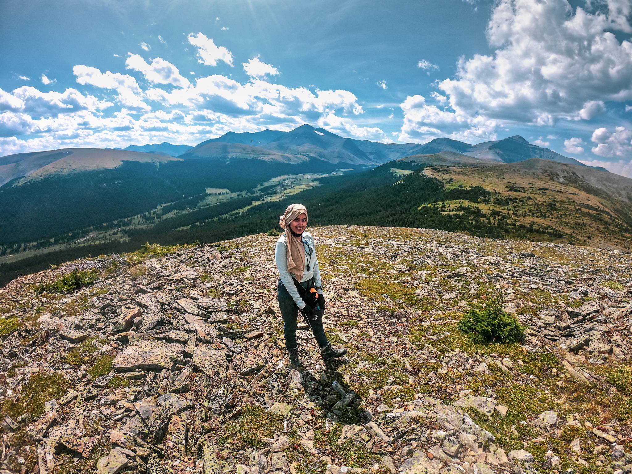 Image of person standing at the top of a mountain overlooking a valley surrounded by moutain peaks.