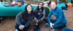 Image of grinning teens sitting in front of canoe