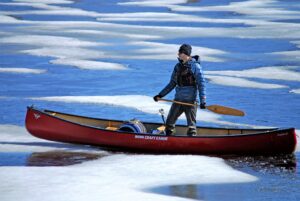 Man standing while canoeing through ice