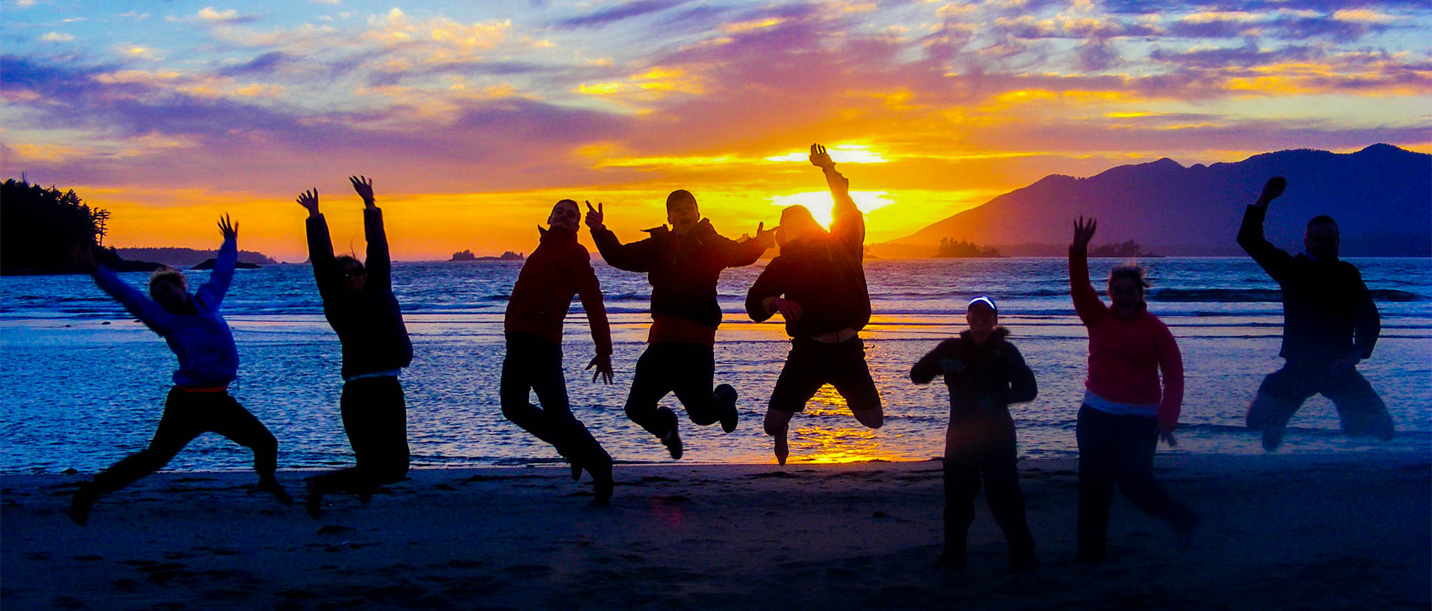 Image of a group, jumping at seashore at dusk
