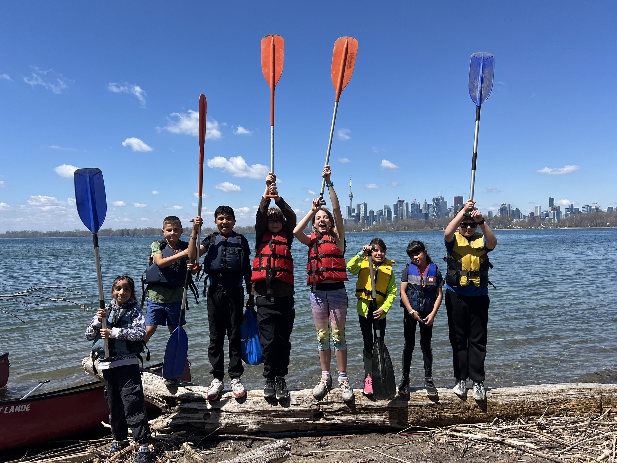 Nature Club for Home Schoolers participants holding paddles by the water with the Toronto skyline in the background.