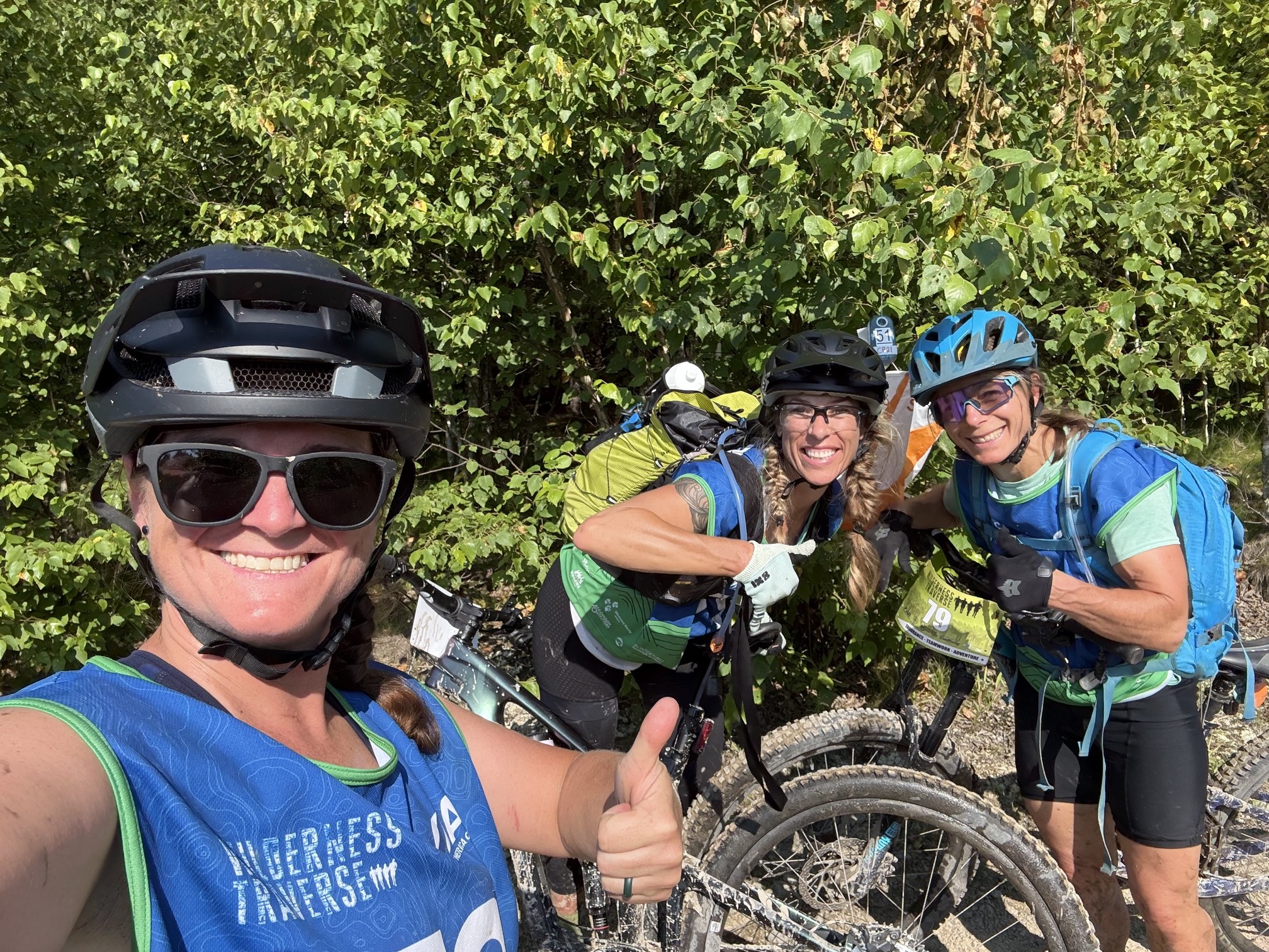 Three members of The Breakfast Club smiling beside their mountain bikes during Wilderness Traverse.