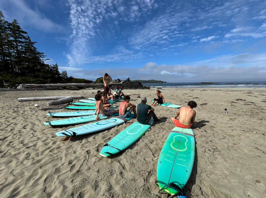A group of participants sit on surfboards during instruction section of the OBC Seak Kayaking and Surf Course in 2024